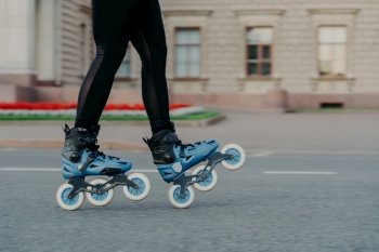 Unrecognizable woman in blue rollerskates moves on road spends free time actively tries new exercise has training poses outdoor near ancient building. Rollerblading as hobby. Active lifestyle