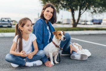 Content family of woman with pretty girl and adorable Jack Russell Terrier sitting on ground. . Happy mother with girl and dog