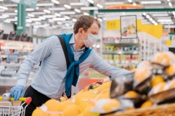 Man wears disposable medical mask and gloves in big supermarket, makes shopping, chooses necessary food products, protects himself from pandemic quarantine. Coronavirus and consumerism concept