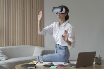 Photo of businesswoman in elegant formal clothes sitting in office and using VR technologies at work, female employee wearing 3d goggles engaged in virtual conference with colleagues. Businesswoman in elegant formal clothes sitting in office and using VR technologies at work