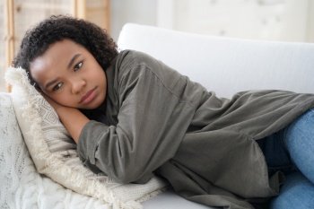 Frustrated lonely teen girl is lying on couch at home. Depressed african american teenager is suffering bullying or violence. Hispanic girl is desperate. Anxiety, stress and health problem concept.. Frustrated lonely teen girl is lying on couch at home. Teenager is suffering bullying or violence.