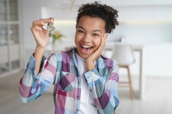 Excited young african american teen girl tenant showing keys of first new house. Happy biracial female delighted with buying or renting apartment holds home key. Relocation, real estate rent service. Excited african american teen girl tenant showing keys of first new house. Real estate rent service