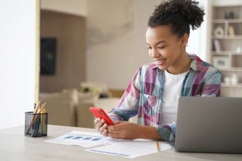 Afro teenage girl is distracting while studying remote. Teenage girl sitting in front of laptop, clicks mobile phone and chatting. African american student gets remote education at school or college.. Afro teenage girl is distracting while studying remote. Student clicks mobile phone and chatting.