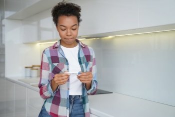 Unwanted pregnancy. Teenage girl gets in trouble with positive pregnancy test result. Frustrated african american young woman is holding stripe test and looking at it. Contraception concept.. Unwanted pregnancy. Frustrated teenage girl gets in trouble with positive pregnancy test result.