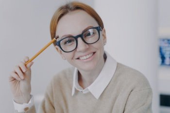 Face of successful attractive girl. Relaxed happy student holding pencil and smiling. Remote study concept. Young european businesswoman or positive manager in glasses.. Face of successful attractive girl. Relaxed happy student holding pencil and smiling. Remote study.