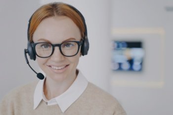 Young lady is consultant of call center. European friendly girl in headset is talking to client in agency. System administrator at workplace. Customer support concept.. Young lady consultant of call center. European friendly girl in headset talking to client in agency.