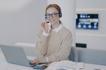 Online interpreter. Young happy woman is consultant of call center. European friendly girl in headset is talking to client in front of laptop. System administrator. Customer support concept.. Online interpreter. Young happy woman in headset is talking to client in front of laptop.