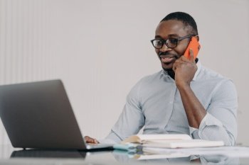 African american businessman talks on phone at laptop in office. Black male manager wearing glasses consulting client, having pleasant conversation with colleague, discussing solving problem distantly. African american businessman talk on phone at laptop, consulting client, discussing business project