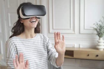 Young excited woman wearing 3d goggles interacting with augmented world, amazed female in VR headset playing games or making purchases in virtual reality store while spending leisure time at home. Young excited woman wearing VR headset interacting with augmented world, playing games at home