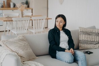 Pensive young woman tired from homework sitting on couch in living room at home. Calm thoughtful female housewife trying to relax on sofa, feeling fatigue after hard work day.. Pensive calm woman tired from homework or work day relax sitting on couch in living room at home