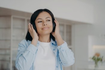 Serene young woman wearing modern wireless headphones listen to favorite music. Female listening to podcast, audio book, audio affirmations, enjoying sound, resting at home. . Woman wearing modern wireless headphones listen to music, podcast, audio book, resting at home