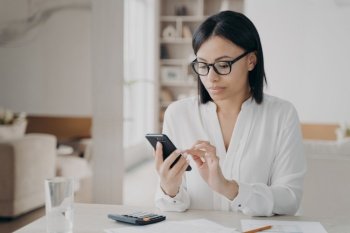 Business lady is appointing meeting, texting on smartphone. Young caucasian businesswoman in glasses and white blouse is working remote from home. Manager, secretary or freelance worker at workplace.. Business lady is appointing meeting, texting on smartphone. Manager or secretary at workplace..