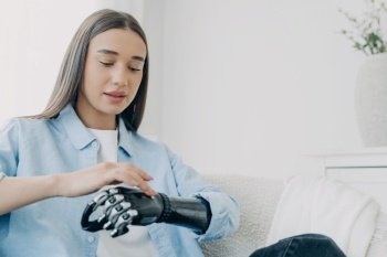 Handicapped girl explores bionic arm, presses buttons. Young European woman with cyber hand at home. Futuristic bionic prosthesis tech.