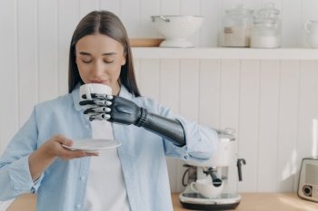 Handicapped person’s routine and life quality. Pretty girl with cyber hand holds tea cup, drinks. Grasp sensors in modern robotic limb. Domestic kitchen scene.