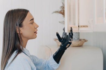 Handicapped girl opens cupboard with cyber hand. European woman with artificial arm. Modern bionic prosthesis functions. Disabled person’s routine.