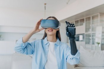 Disabled person undergoes rehabilitation. Handicapped girl uses cyber arm with VR goggles at home.