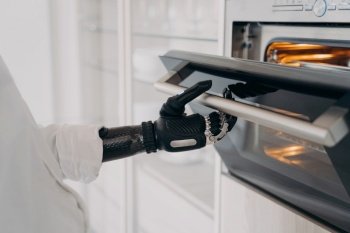 Handicapped person’s robotic cyber hand opens oven in the kitchen, ready to bake.