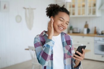 Modern young mixed race girl enjoys her music, holding a smartphone and using musical apps to enhance her home listening experience.