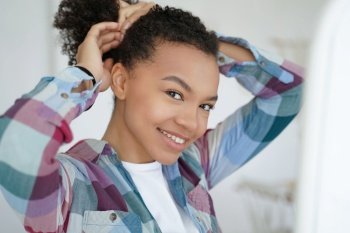 Smiling young mixed race girl embraces her natural beauty, holding and styling her healthy afro hair with care and self-love.