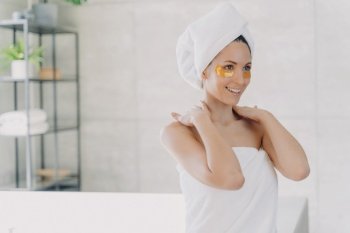 Woman with eye patches enjoys skincare routine in bathroom after shower.