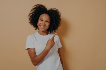 Smiling African female model in white shirt pointing with finger at blank copy space, advertising concept.