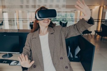 Smiling businesswoman in casual clothes dodging in VR, immersed in digital world with portable glasses, empty office.
