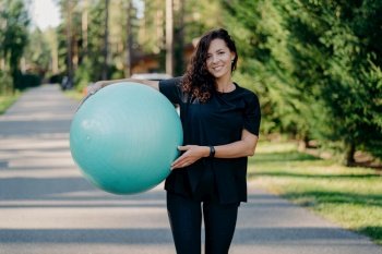 Fitness trainer with fitball, outdoors, dressed in sportswear, walking near forest road, preparing for a masterclass for pregnant women.