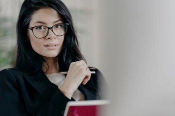 Confident female employee in formal wear writes notes, plans, and works on project, wearing glasses.