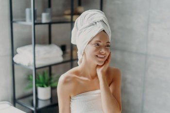Smiling spa lady with natural makeup poses refreshed after shower, touches healthy skin in bathroom.