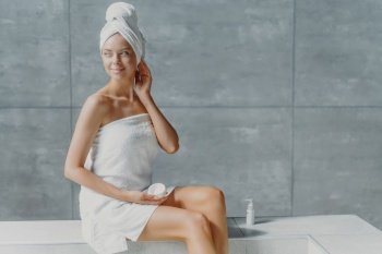 Thoughtful woman applies body cream, bare shoulders, clean skin, enjoys spa.