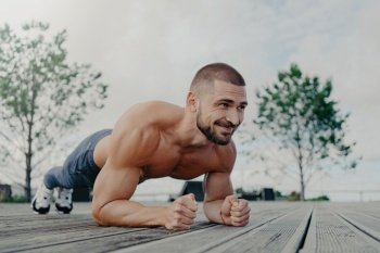 Fit bearded man in plank pose, smiles outdoors. Focuses on health and fitness.