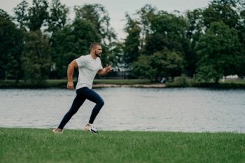 Active bearded man runs against nature, prepares for marathon, captures the moment in motion. Sport and wellness concept.