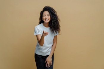 Energetic woman with curly Afro hair, pointing forward at camera, positive and decisive, white t-shirt, jeans. Noticing something nice ahead.