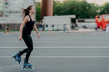Energetic woman rollerblades on city road, smiling. Dark hair in the wind. Active lifestyle. Outdoor photo