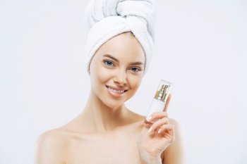 Smiling woman with cosmetic product, cared skin, towel on head, enjoys rejuvenation treatment