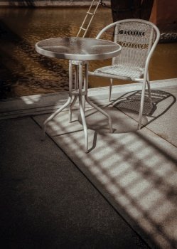 Sunbeam shine through the bridge and refect the white metal chair and the table with river view in the sunny day with good atmosphere, Space for text, Selective focus.