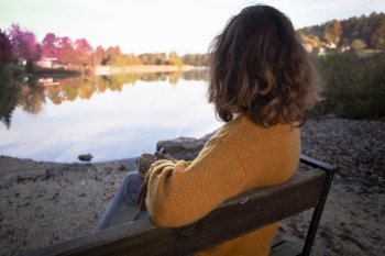 girl with a cup of coffee sits on the shore of the lake
