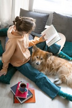 happy girl and corgi. a girl sits on the floor and reads a book next to a corgi dog
