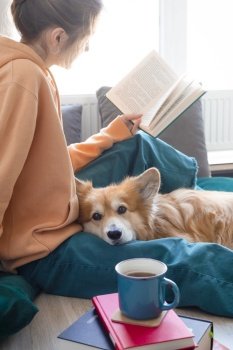 happy girl and corgi. a girl sits on the floor and reads a book next to a corgi dog

