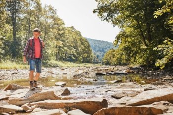 Trekking with backpack concept image. Backpacker wearing trekking boots crossing mountain river. Man hiking in mountains during summer trip. Vacation trip close to nature. Natural scenery