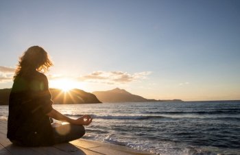 woman meditating by the sea at sunset