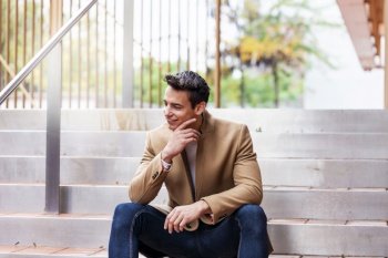 Portrait of stylish young man with coat sitting on a stairs
