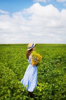 beautiful girl stands in the field with a bouquet of yellow flowers and a straw hat.. beautiful girl stands in the field with a bouquet of yellow flowers and a straw hat