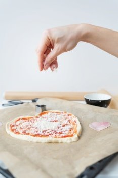 Pizza dough in the shape of a heart, the chef sprinkles the pizza with parmesan cheese. The concept of a surprise for St. Valentine’s Day. Pizza dough in the shape of a heart, the chef sprinkles the pizza with parmesan cheese. The concept of a surprise for St. Valentine’s Day.