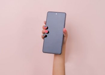 Girl hand holding smartphone on pink background in studio. Mobile phone mockup for your product.