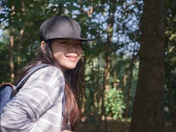 Happy young Asian woman with backpack walking on path in summer forest.
