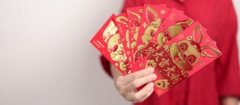 Woman holding Chinese red envelope with golden rabbit and blessing word, money gift for happy Lunar New Year holiday. Chinese sentence means happiness, healthy, Lucky and Wealthy