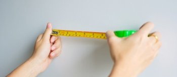 Man hand using tape measure for measuring with wall backgrounds at home. DIY, Interior design, repairing and improvement home or apartment concepts