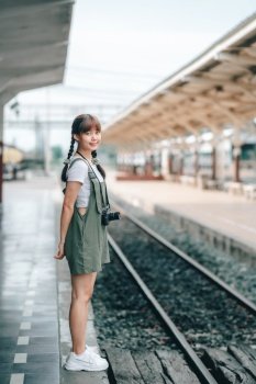 Portrait Young asian woman smiling tourist Traveler girl walking and with a holding the camera waits train travel journey is taken in railway platform Thailand, summer relax vacation Concept.