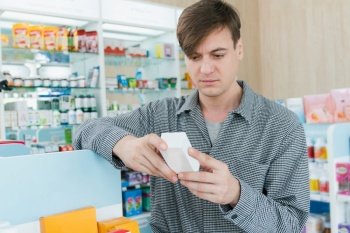 Young thoughtful caucasian man reading medicine, medical label product before decide buying from qualified pharmacy. Customer choice concept in drugstore.. Thoughtful caucasian man reading qualified medical label product before buying.